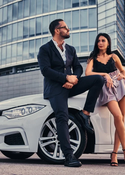 well-dressed-attractive-couple-leaning-luxury-car-outdoors-against-skyscraper (1) Premium vs Luxury Car