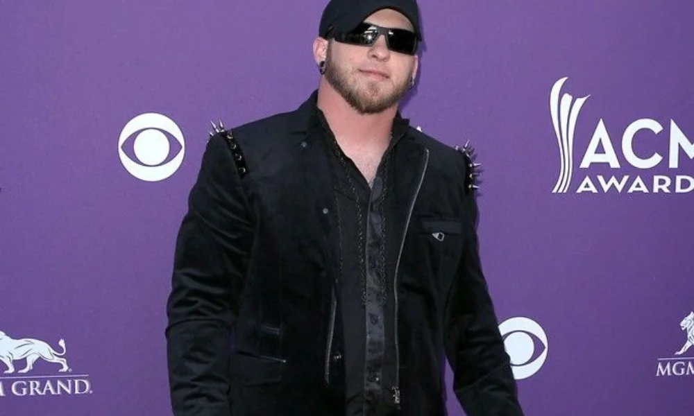Man in a studded black jacket and sunglasses stands confidently 