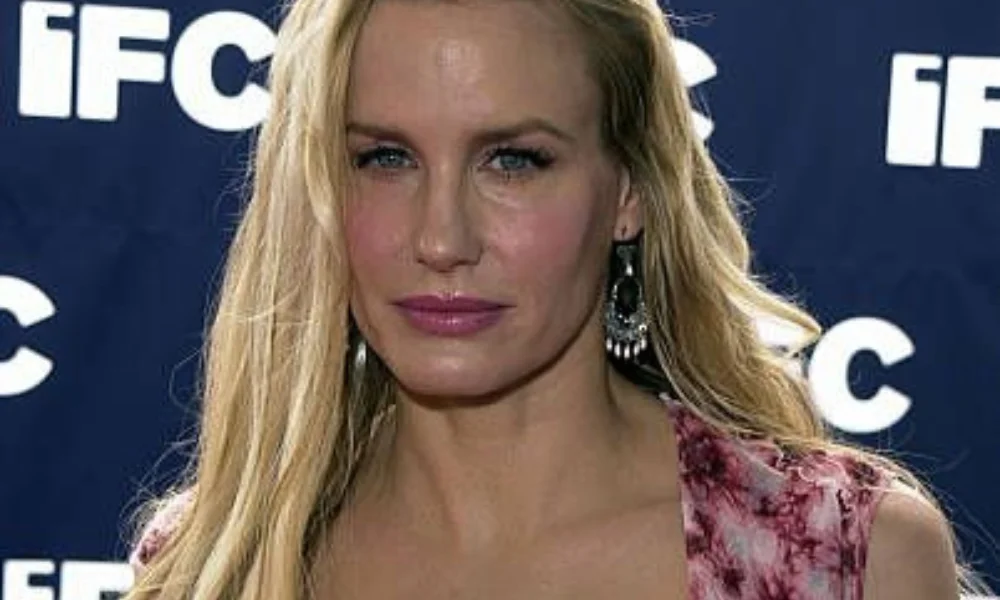 woman with long blonde hair stands against a backdrop