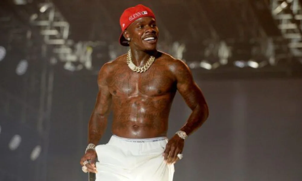 A shirtless performer wearing a red cap and white pants on stage-dababy's net worth