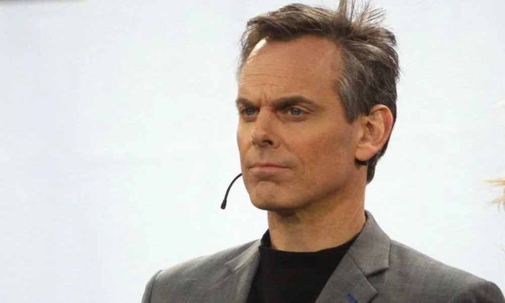 A person wearing a gray suit and black shirt-colin cowherd net worth