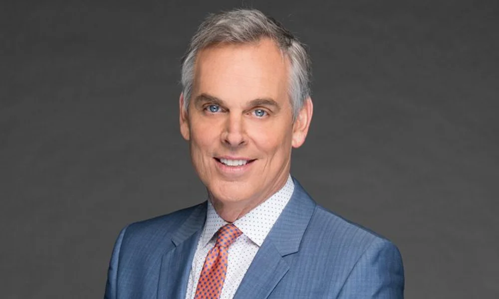 Smiling man in a blue suit and red tie against a gray background
