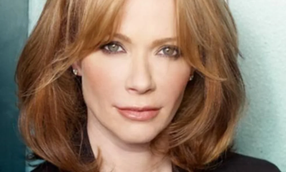 A person with shoulder-length auburn hair, wearing a black top-lauren holly's net worth