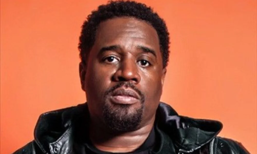 A person in a black leather jacket against an orange background-corey holcomb net worth