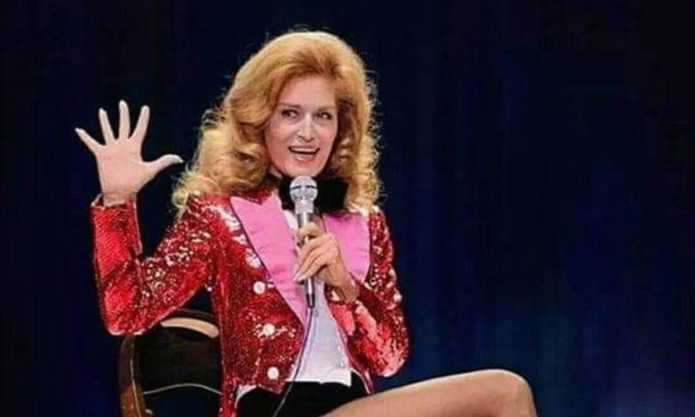 A person with long hair, wearing a sparkling red blazer with pink lapels