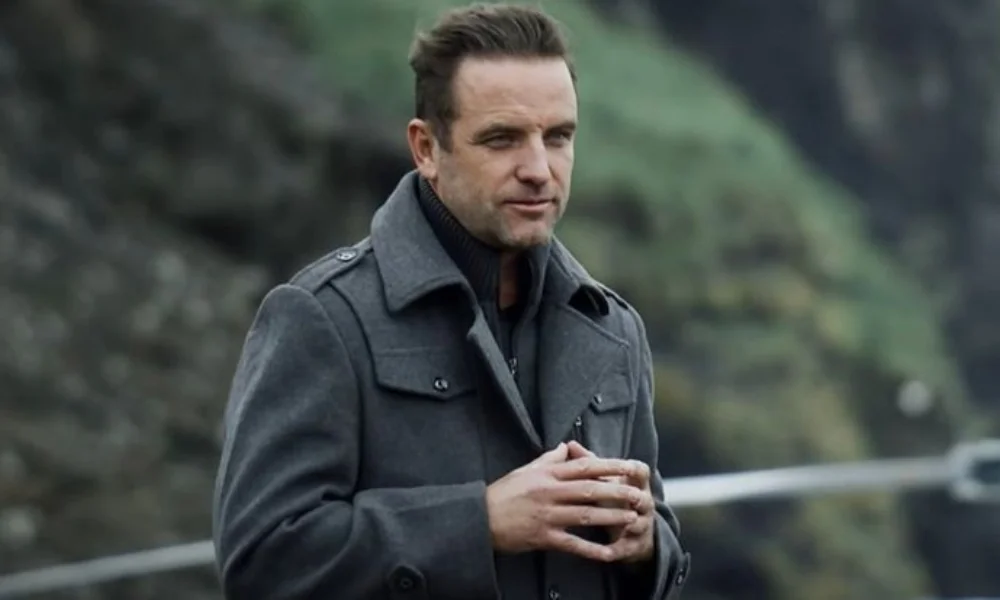 A man in a gray coat stands outdoors-tj lavin net worth