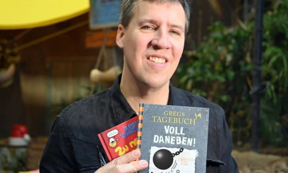 A person holding books titled "Gregs Tagebuch" and "Zu nett,"-jeff kinney net worth