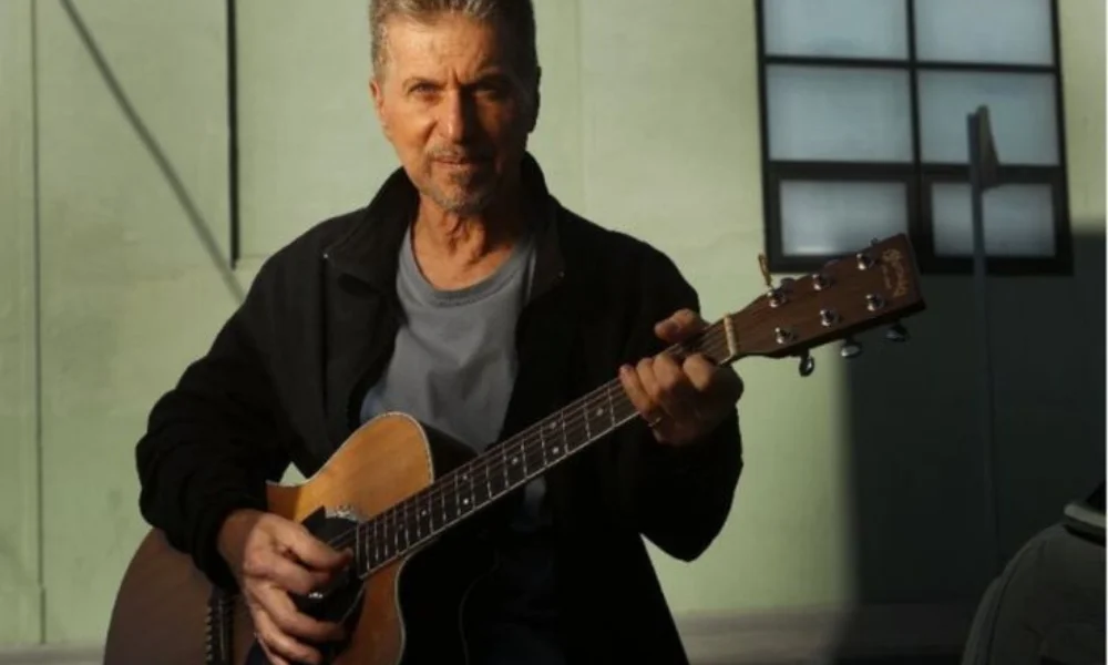 Man playing an acoustic guitar outdoors in sunlight-johnny rivers net worth