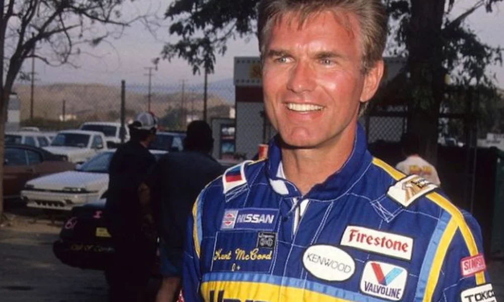 Smiling man in a blue and yellow race suit with sponsor logos