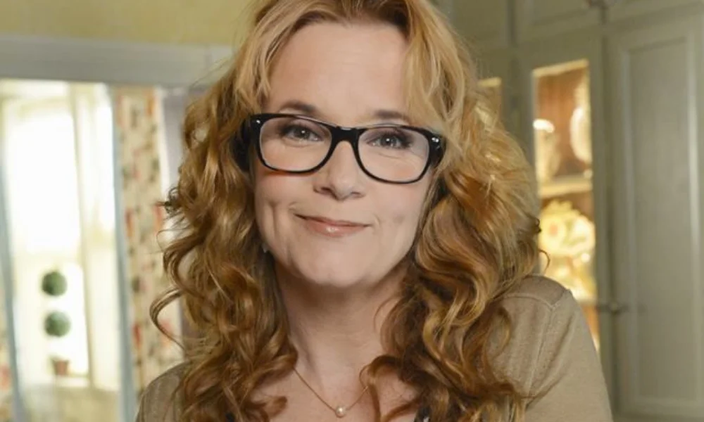 Smiling woman with wavy blonde hair and black glasses-lea thompson net worth