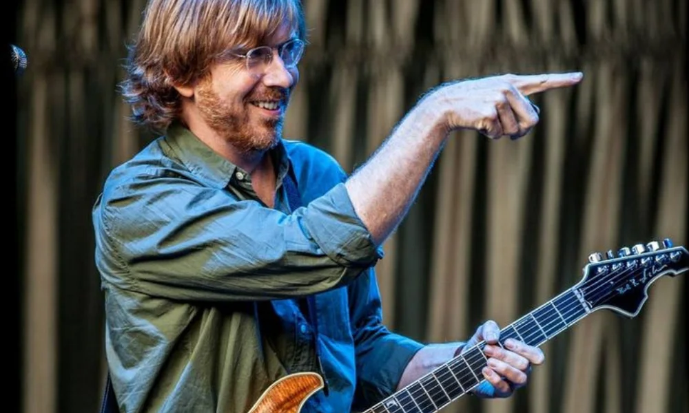 Smiling musician with glasses and a beard points while holding a guitar