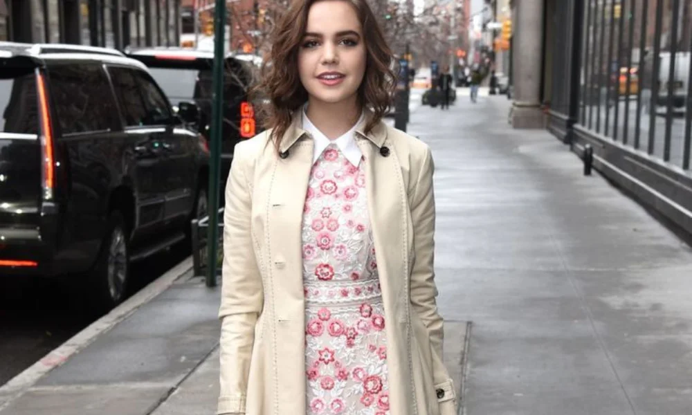 Young woman with wavy hair walks down a city sidewalk