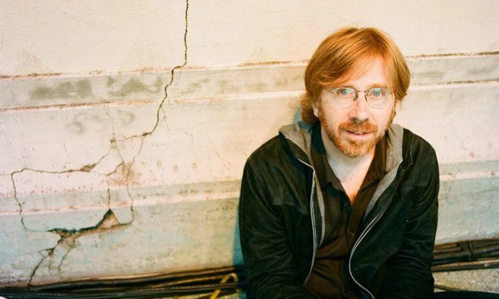 A man with glasses and red hair sits against a cracked wall-trey anastasio net worth