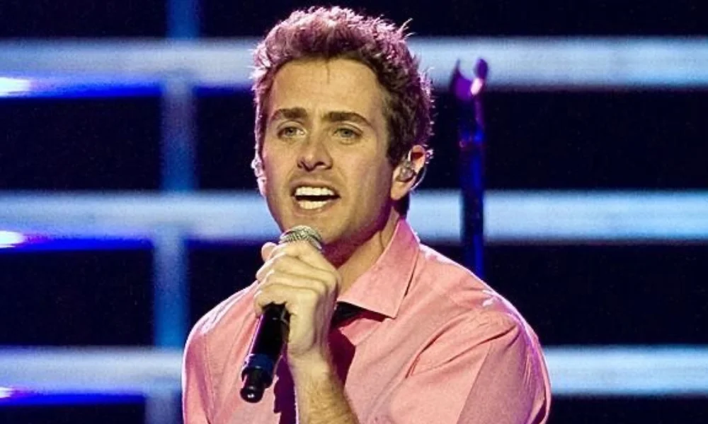 A man passionately sings into a microphone on stage-joey mcintyre net worth
