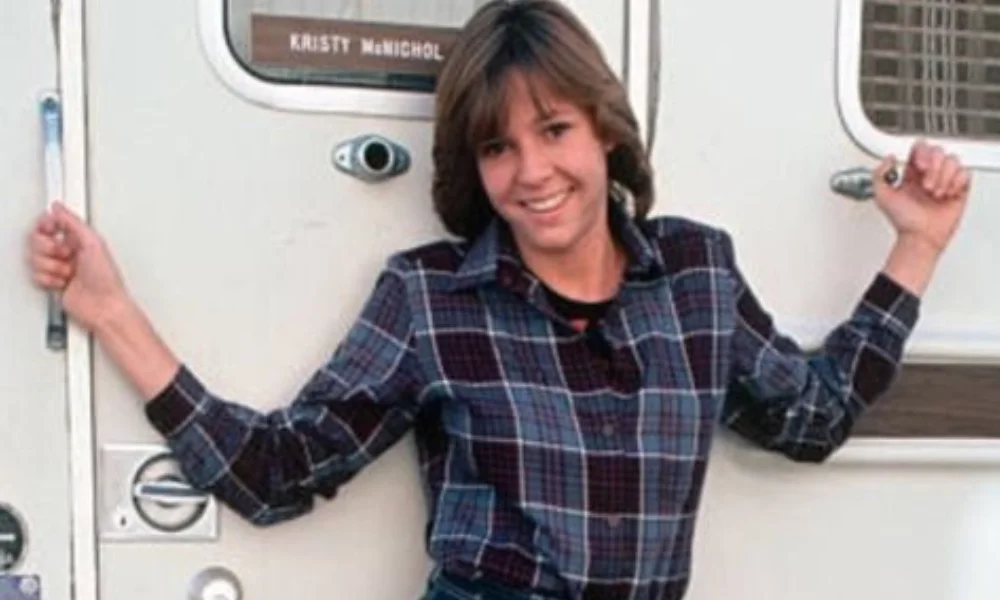 A person stands smiling in front of a white vehicle-kristy mcnichol net worth