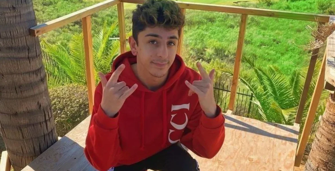 Young man in a red hoodie makes a playful hand gesture while sitting on a platform
