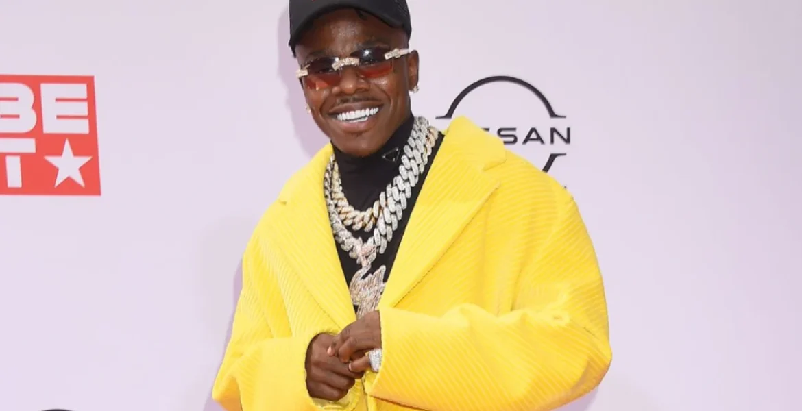 Man smiling on the red carpet, wearing a bright yellow coat, black cap, sunglasses