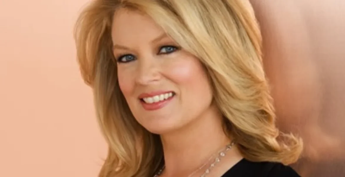 Smiling woman with blonde hair wearing a black top and necklace