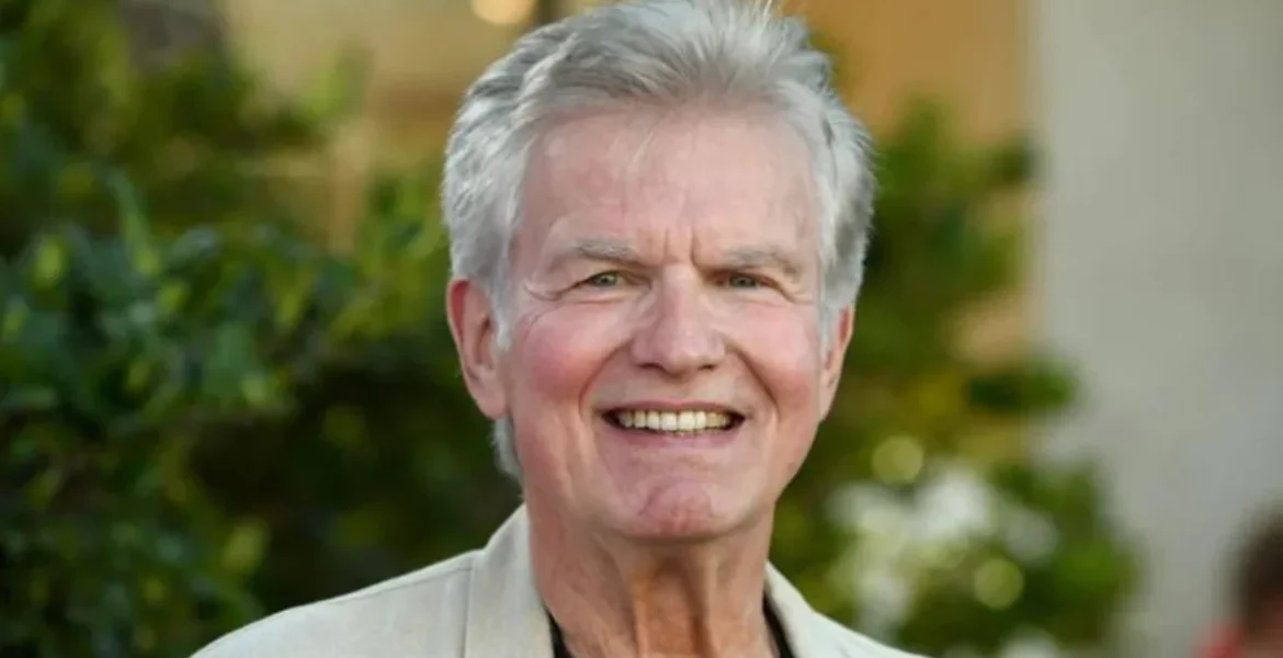 A smiling older man with white hair stands outdoors