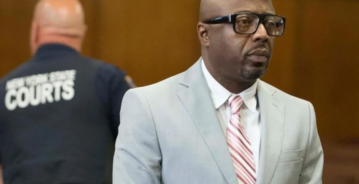 A man in a gray suit and striped tie stands in a courtroom