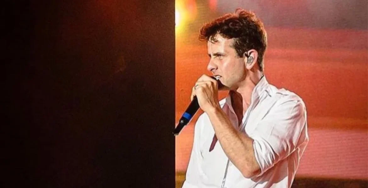 A singer in a white shirt passionately performs on stage