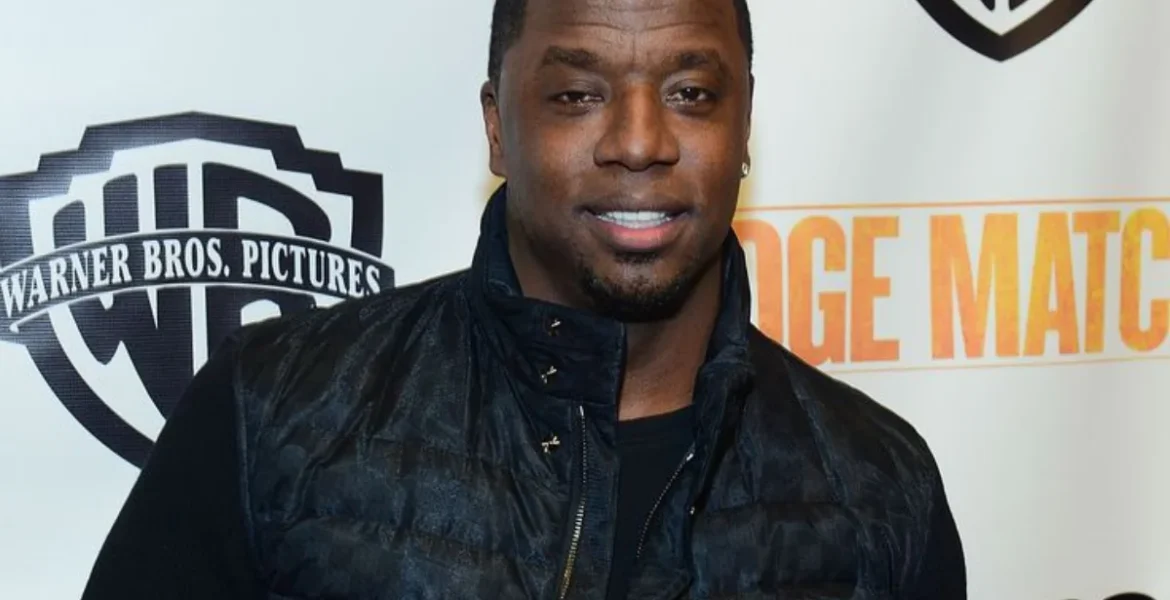 Smiling man in a dark jacket against a backdrop featuring the Warner Bros