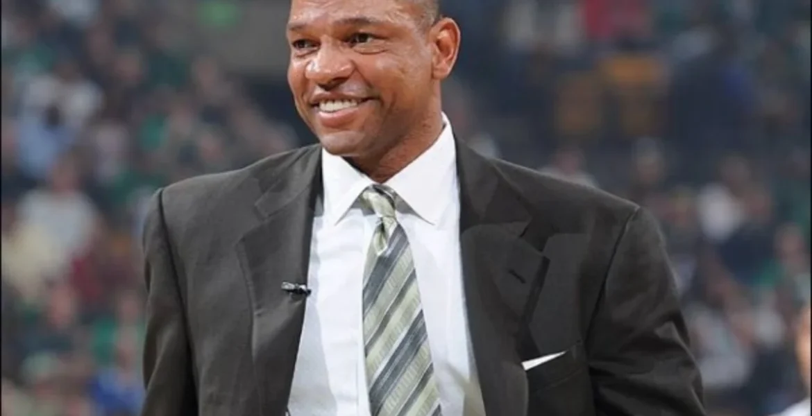A man in a dark suit and striped tie smiles warmly