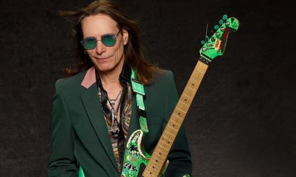 Man in green suit and sunglasses holding a green electric guitar-steve vai net worth