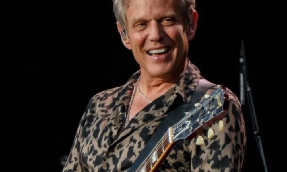 Smiling musician in a leopard-print shirt plays an electric guitar-don felder net worth