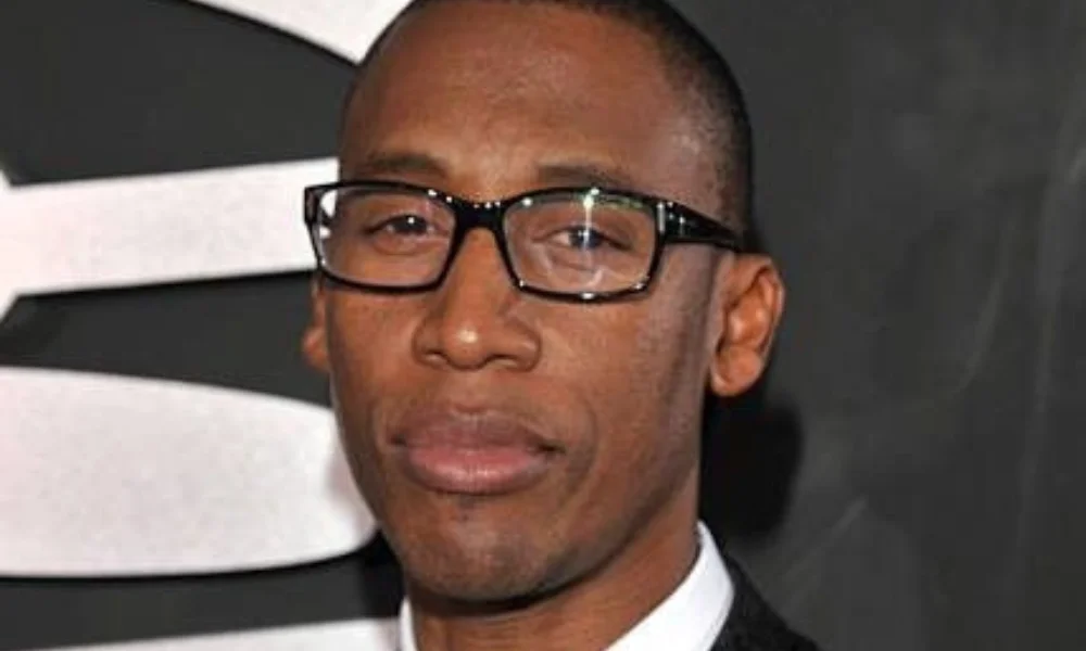A person wearing black-rimmed glasses and a suit-raphael saadiq net worth