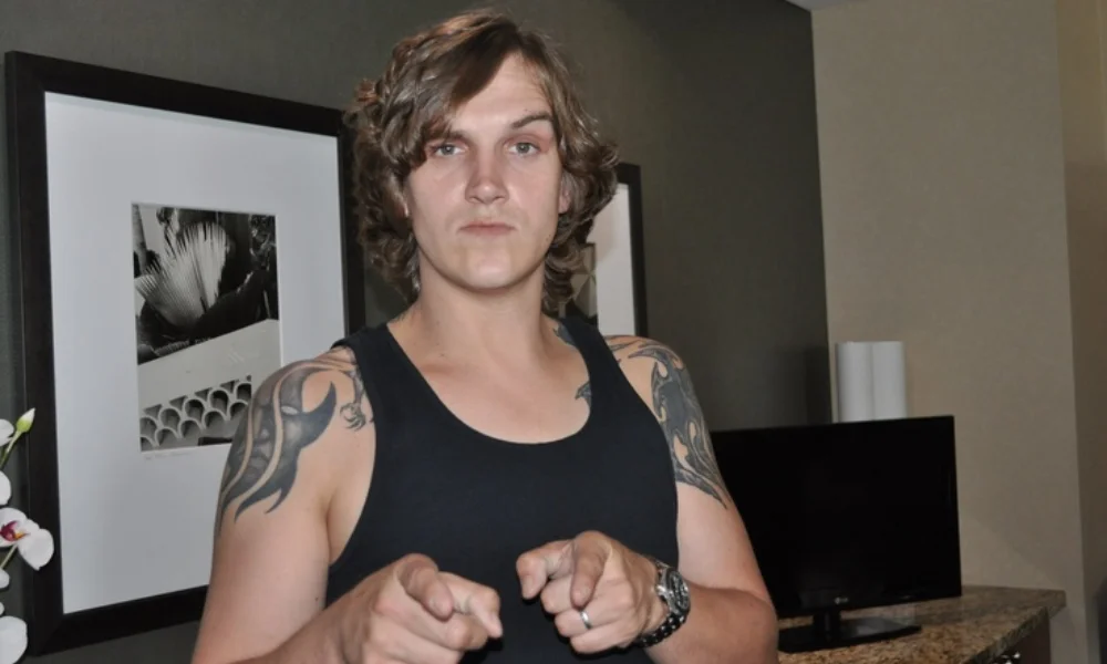 Young person in a black tank top with tattooed arms