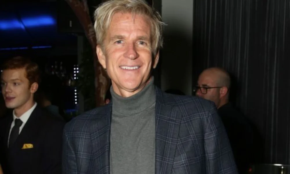 Smiling man in a plaid blazer and gray turtleneck at an indoor event-matthew modine net worth
