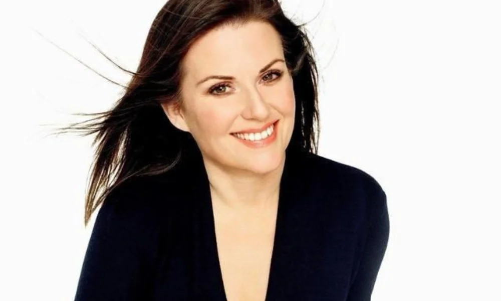 A smiling person with long brown hair and a black top