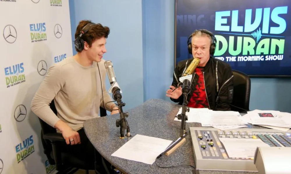 Two people are seated at microphones in a radio studio setting-elvis duran net worth