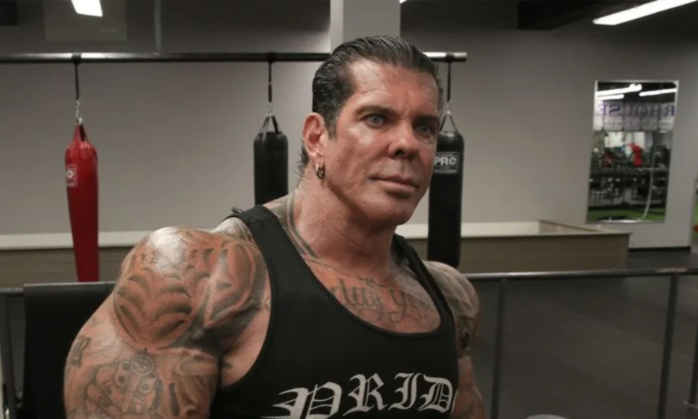 Muscular man in gym, wearing a black tank top with tattoos on arms-rich piana net worth
