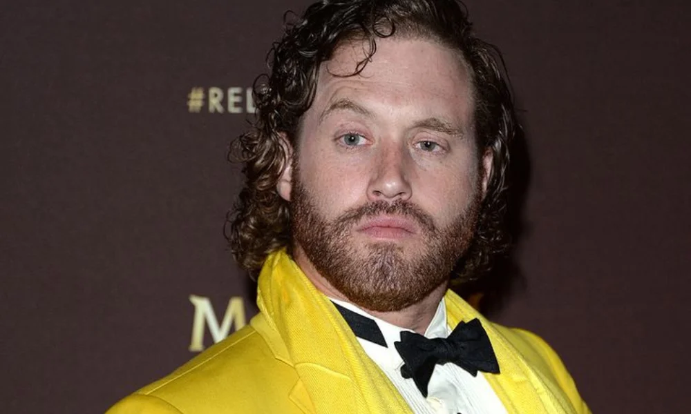 A person with curly hair and a beard wears a bright yellow suit-tj miller net worth