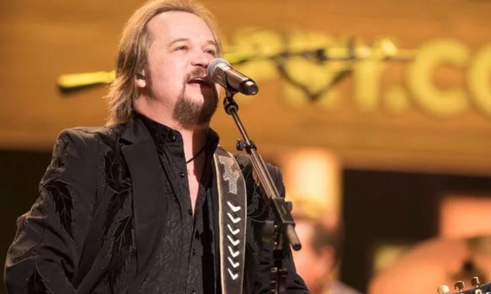 A man with a goatee sings into a microphone on stage-travis tritt net worth