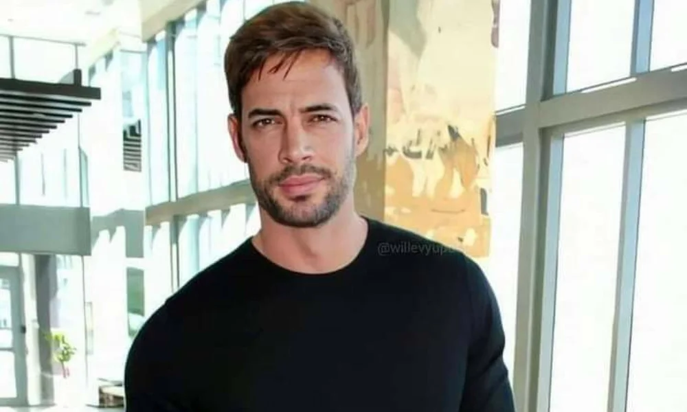 A man with short hair and a beard stands confidently indoors
