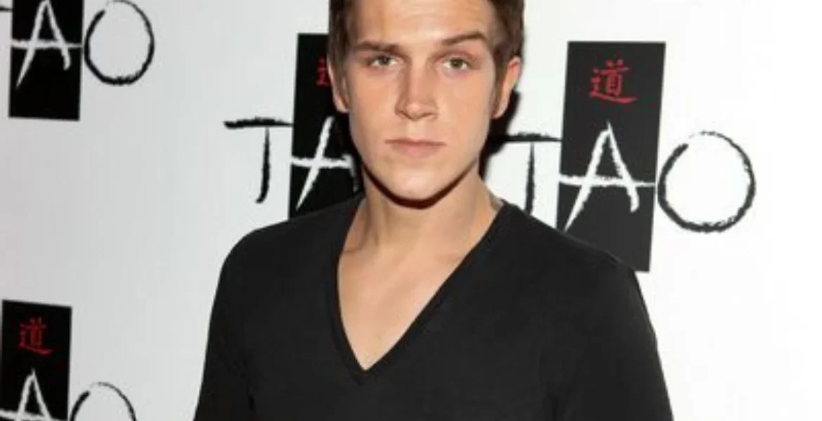 A person with short brown hair in a black V-neck shirt