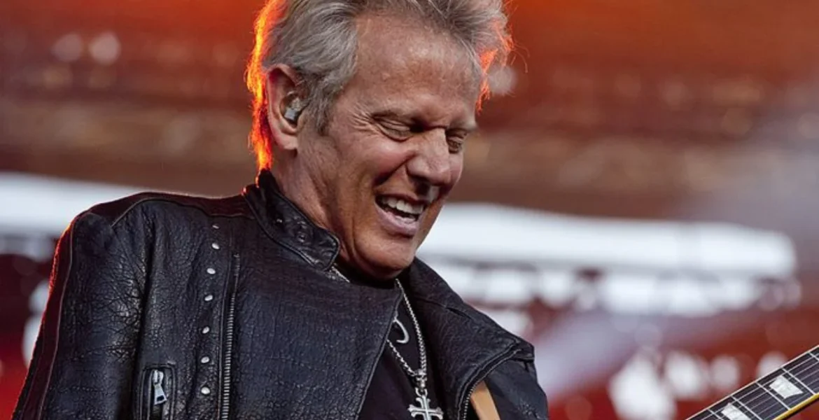 A musician with blonde hair passionately plays a guitar on stage