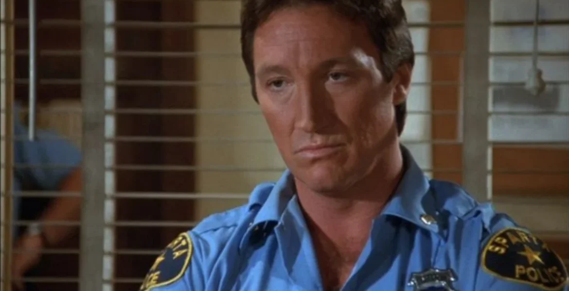 A man in a blue police uniform sits behind metal bars