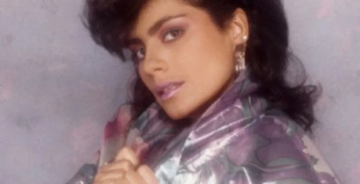 A woman with dark, voluminous hair poses confidently